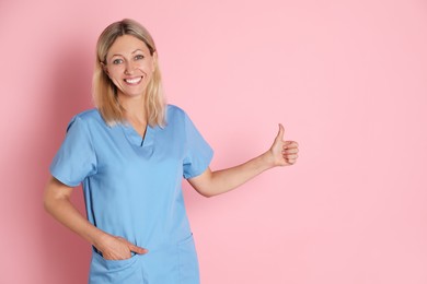 Nurse in medical uniform showing thumbs up on pink background