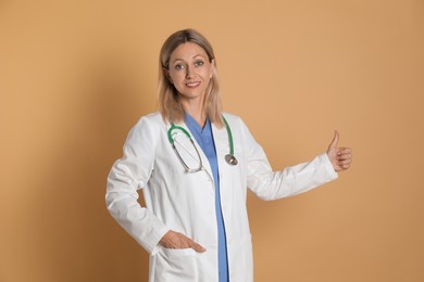 Doctor in medical uniform with stethoscope showing thumbs up on beige background