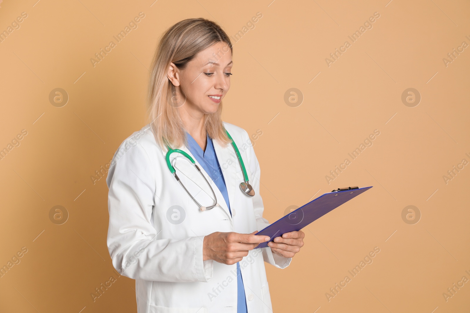 Photo of Doctor in medical uniform with stethoscope and clipboard on beige background