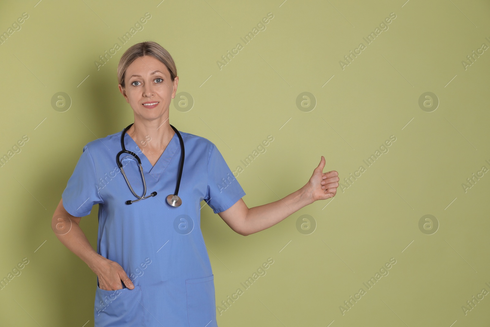 Photo of Nurse in medical uniform with stethoscope showing thumbs up on light green background