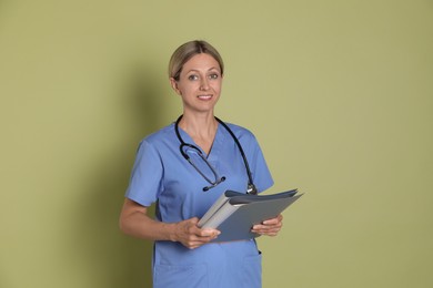 Portrait of nurse in medical uniform with folders on light green background