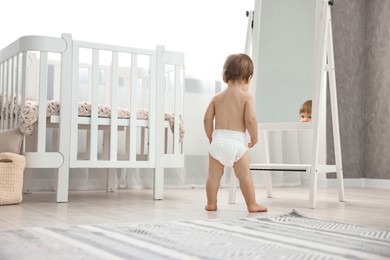 Photo of Little child in diaper near mirror at home