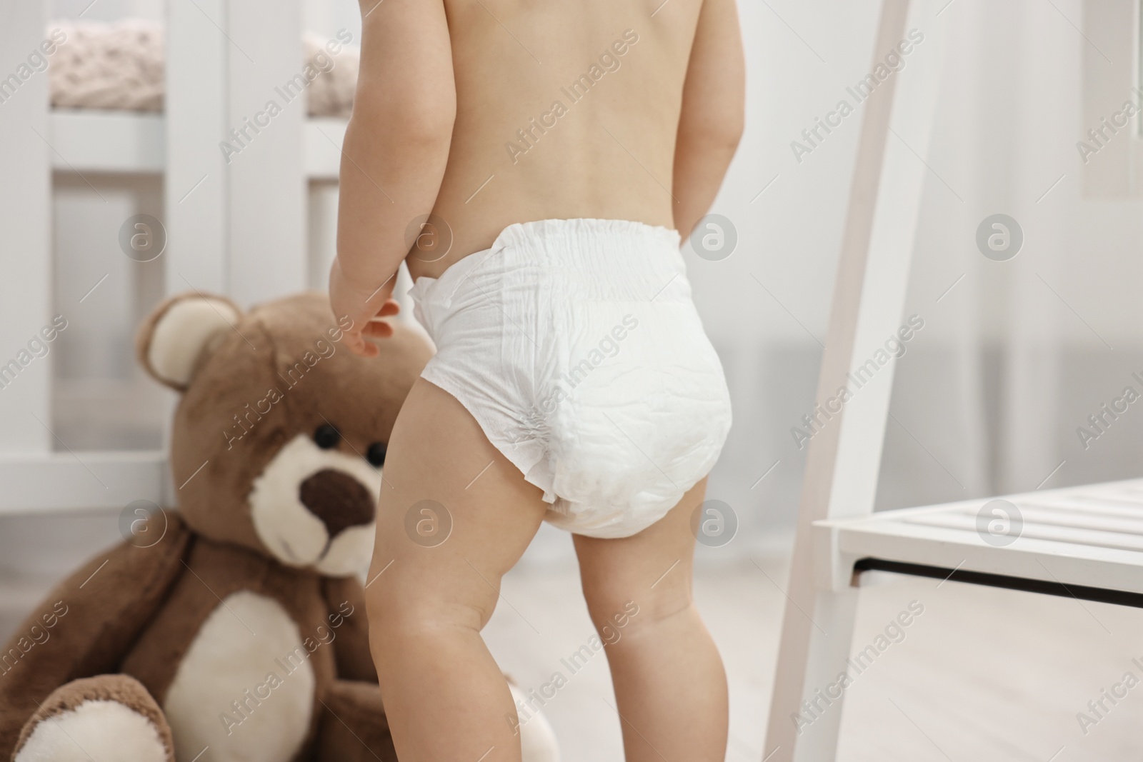 Photo of Little child in diaper with teddy bear at home, closeup