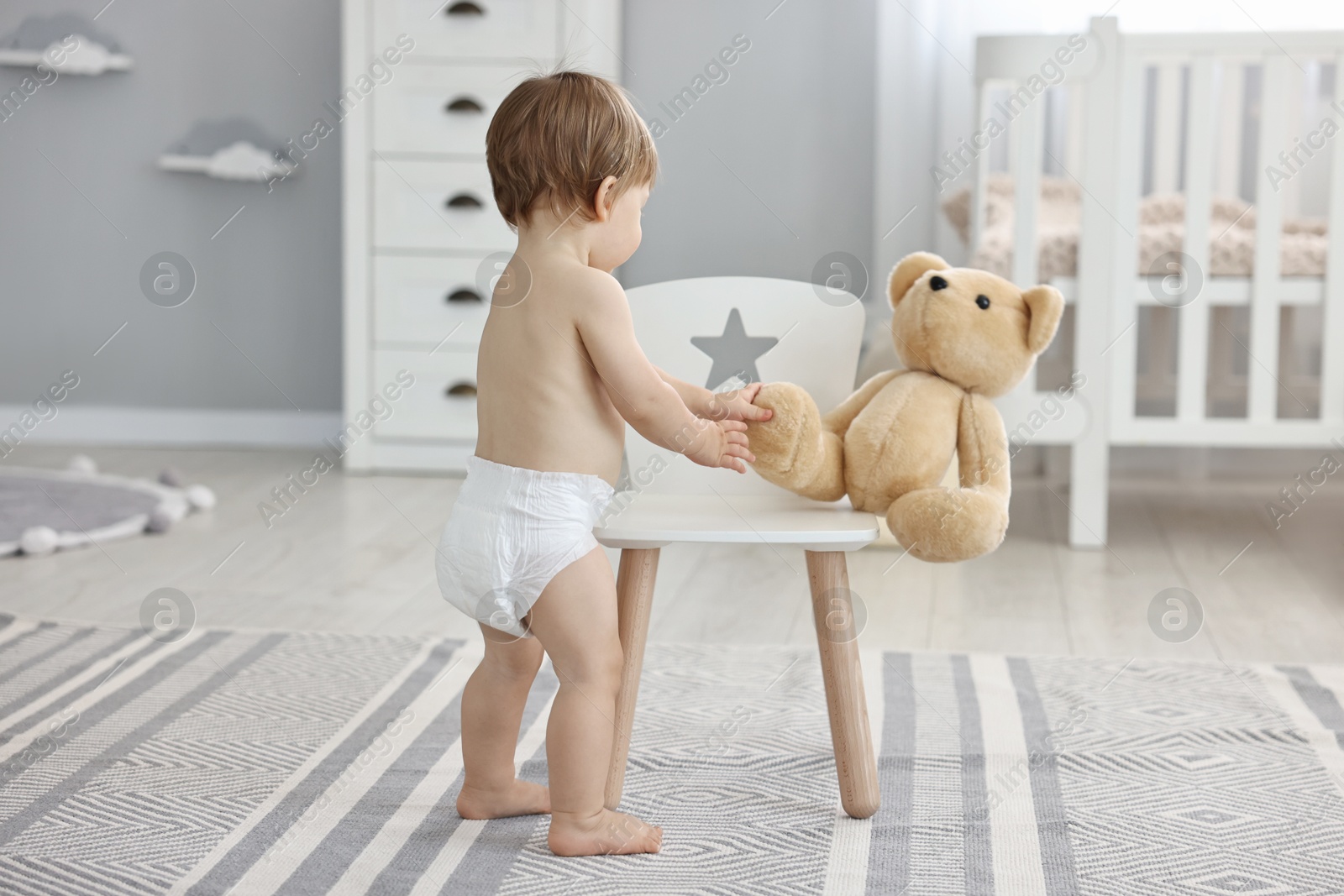 Photo of Little child in diaper with teddy bear at home