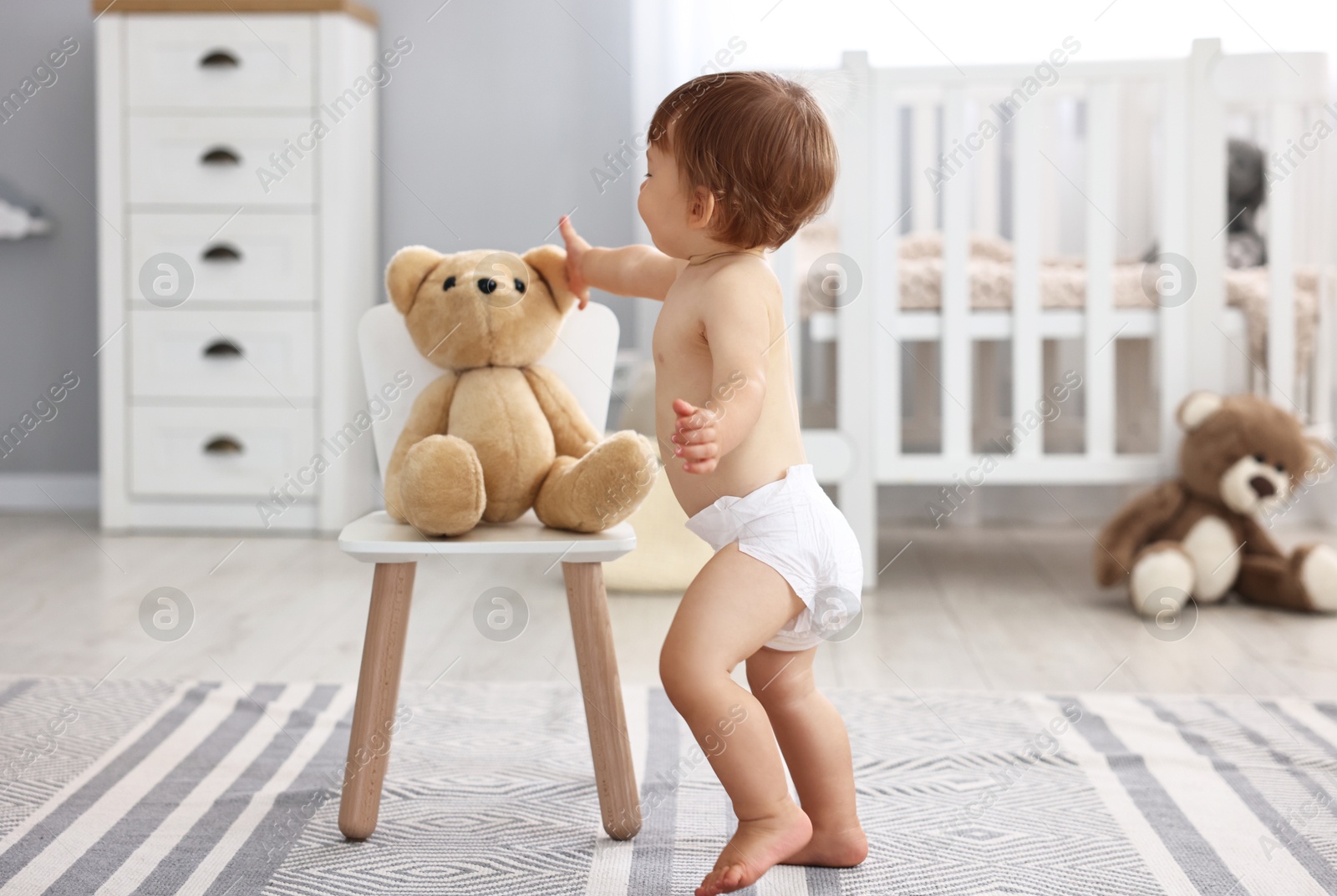 Photo of Little child in diaper with teddy bear at home