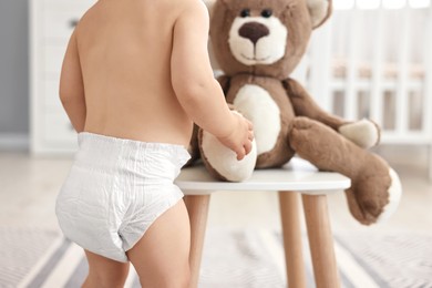 Photo of Little child in diaper with teddy bear at home, closeup