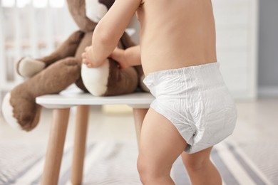 Photo of Little child in diaper with teddy bear at home, closeup