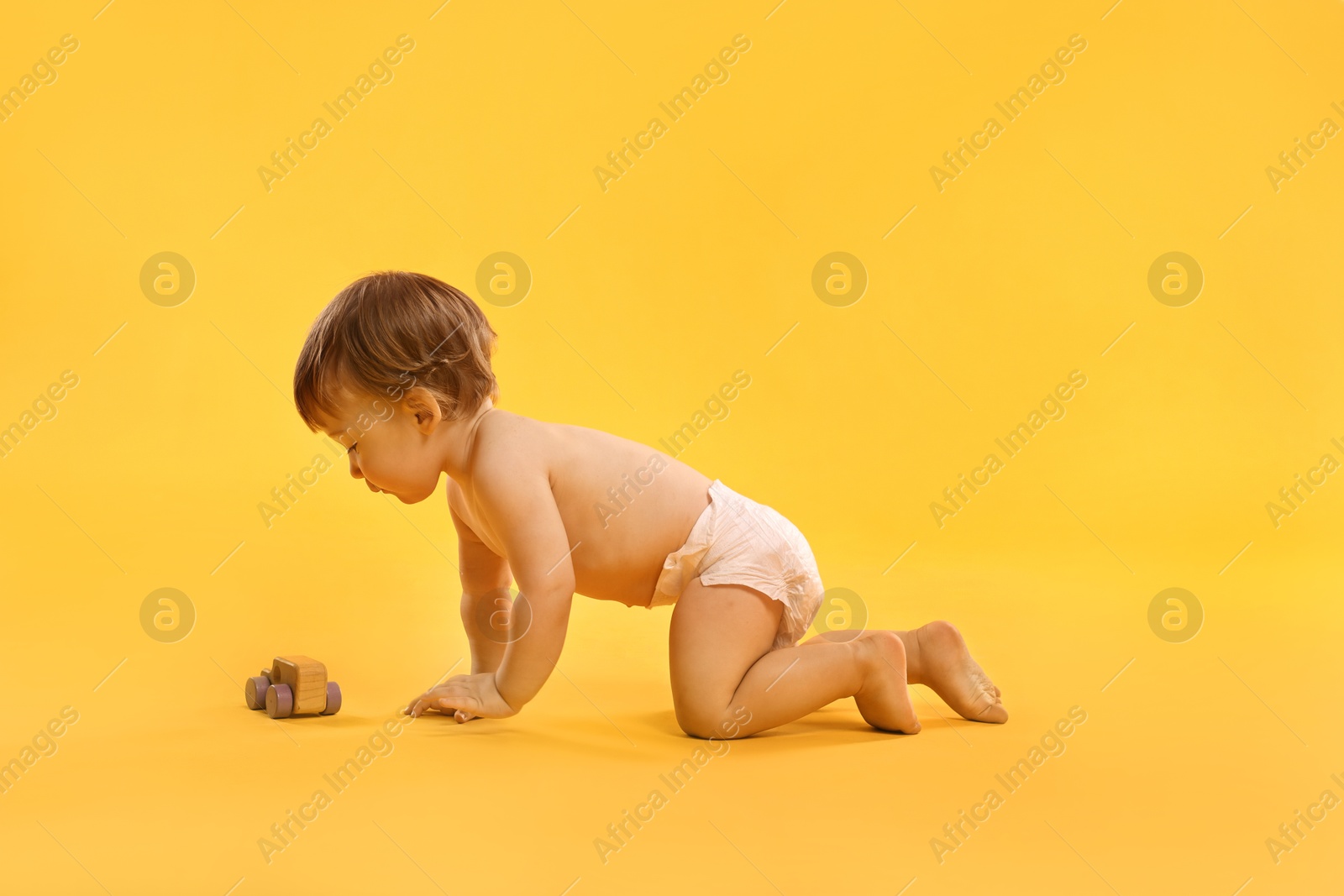 Photo of Little child in diaper with toy on orange background