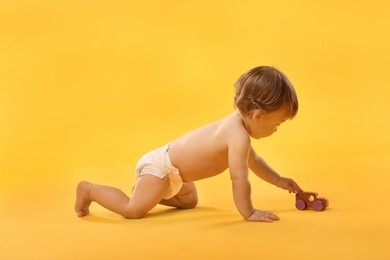 Photo of Little child in diaper with toy on orange background