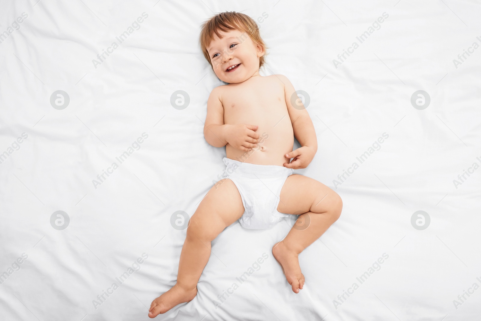 Photo of Little child in diaper on bed, top view