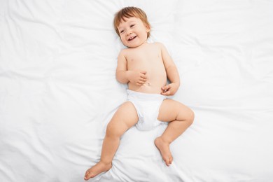 Photo of Little child in diaper on bed, top view