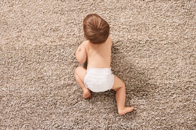 Photo of Little child in diaper on carpet indoors, top view