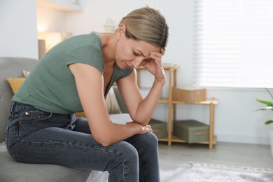 Menopause. Woman suffering from headache on sofa at home