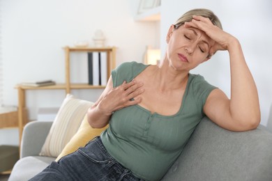 Photo of Menopause. Woman suffering from hot flash on sofa indoors