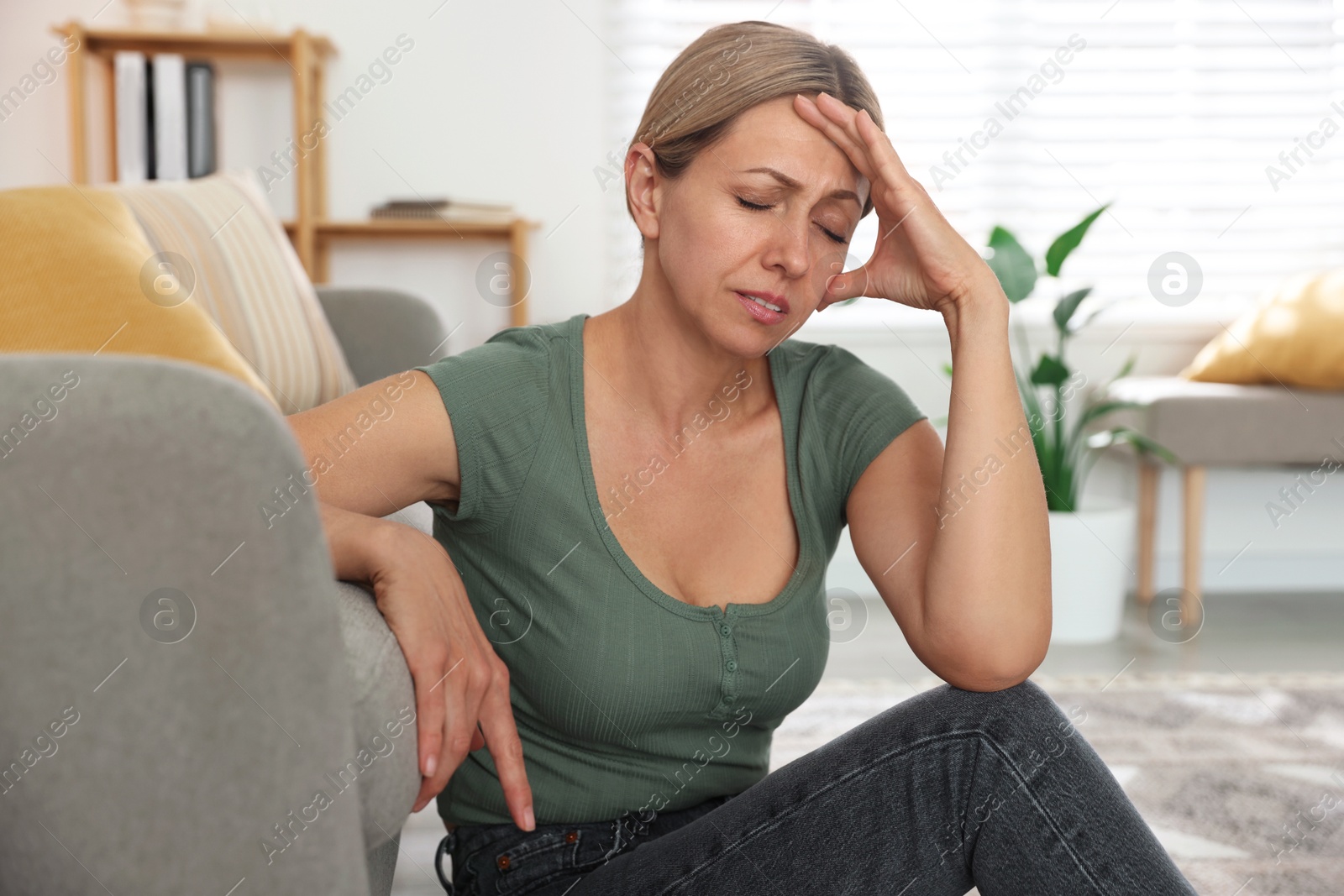 Photo of Menopause. Woman suffering from headache on floor indoors