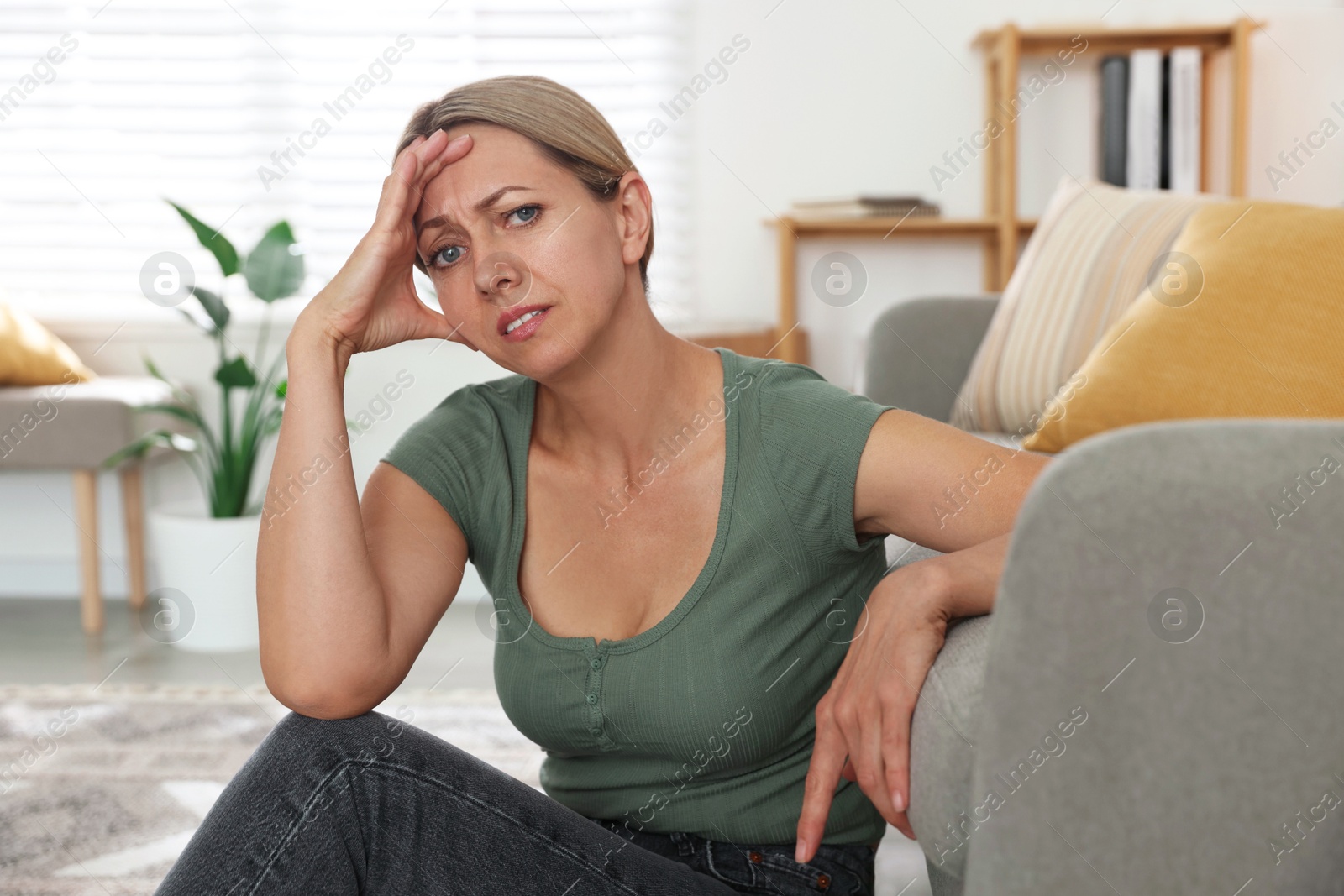 Photo of Menopause. Woman suffering from headache on floor indoors