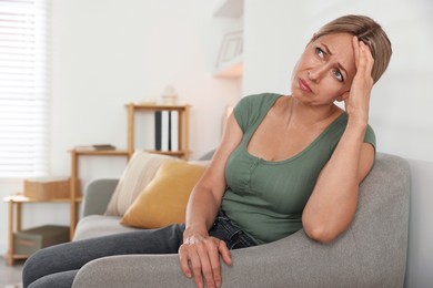 Photo of Menopause. Woman suffering from headache on sofa at home