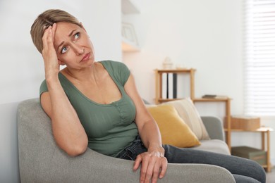 Photo of Menopause. Woman suffering from headache on sofa at home