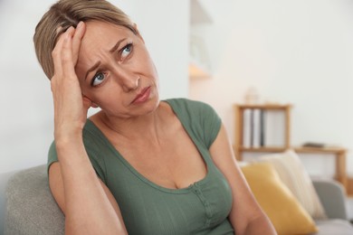 Photo of Menopause. Woman suffering from headache on sofa at home