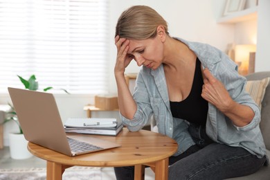 Photo of Menopause. Woman suffering from hot flash at table with laptop indoors