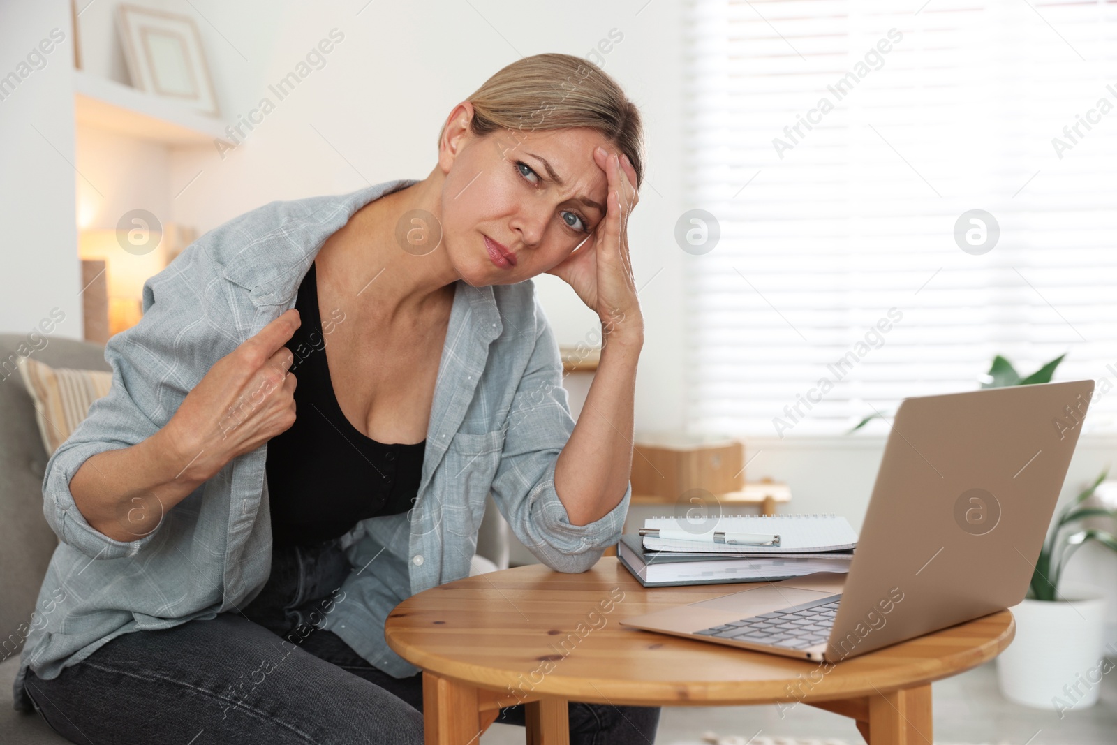 Photo of Menopause. Woman suffering from hot flash at table with laptop indoors