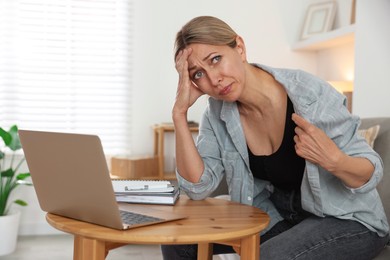 Photo of Menopause. Woman suffering from hot flash at table with laptop indoors