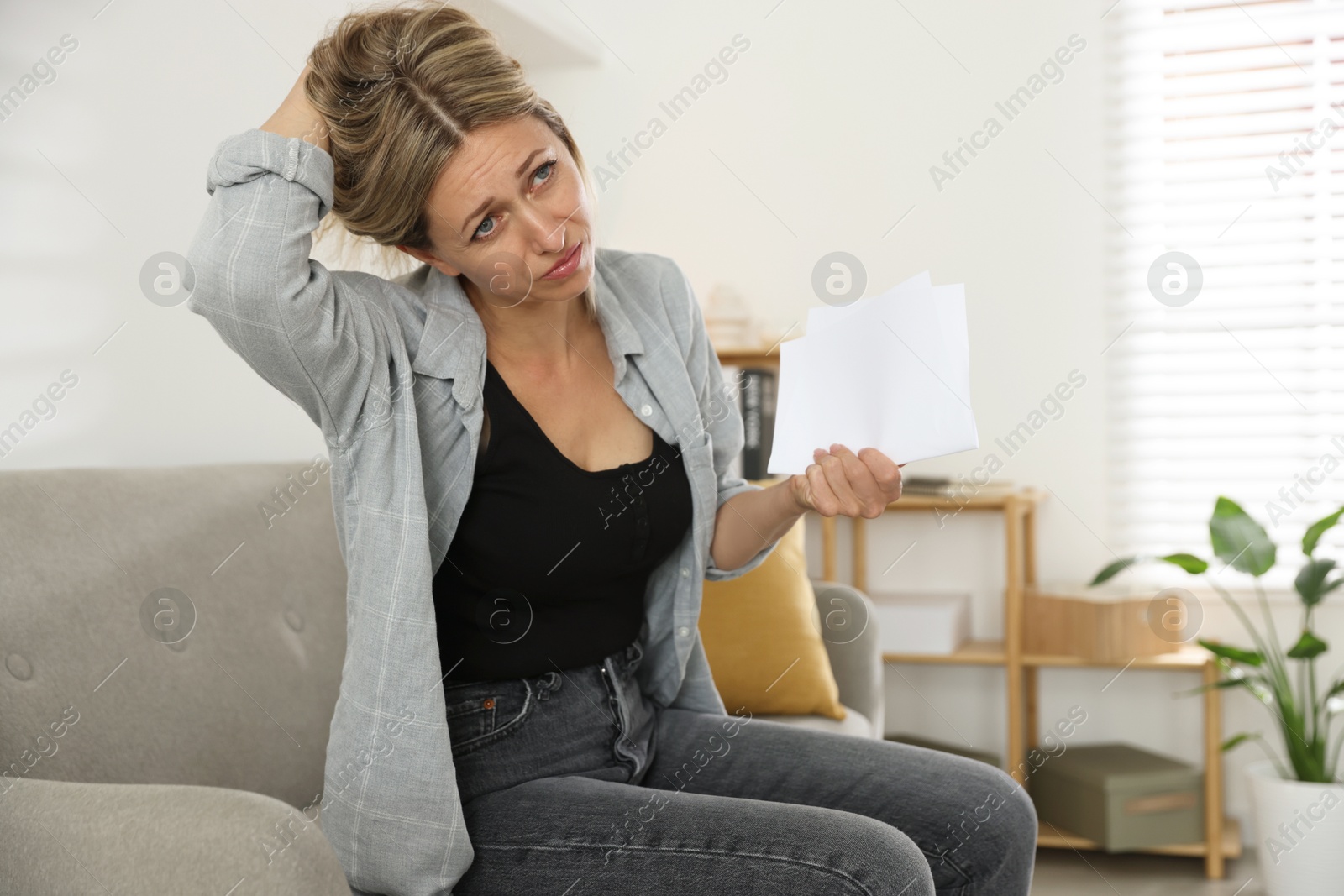 Photo of Menopause. Woman waving paper sheet to cool herself during hot flash on sofa at home