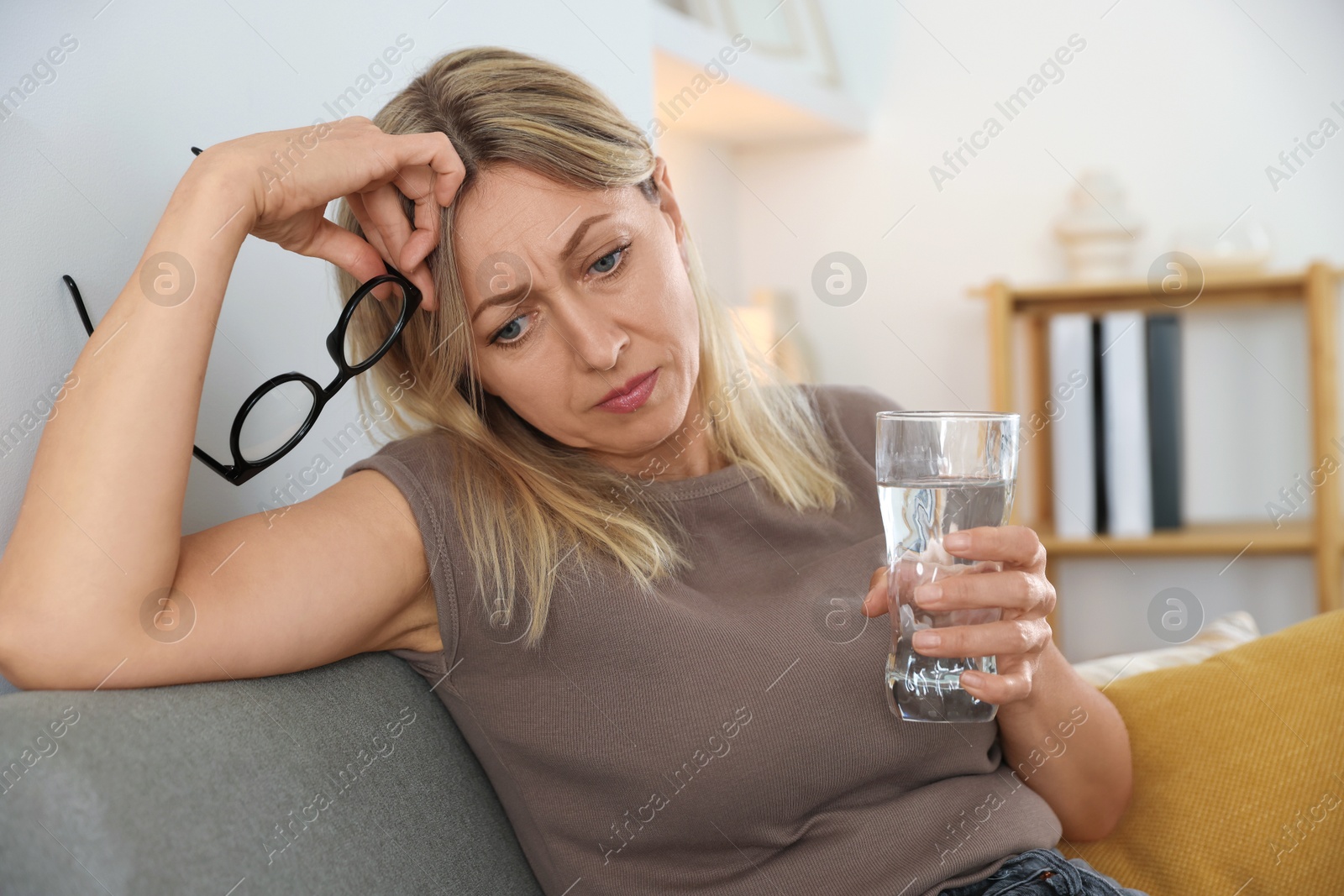 Photo of Menopause. Woman with glass of water suffering from headache on sofa at home