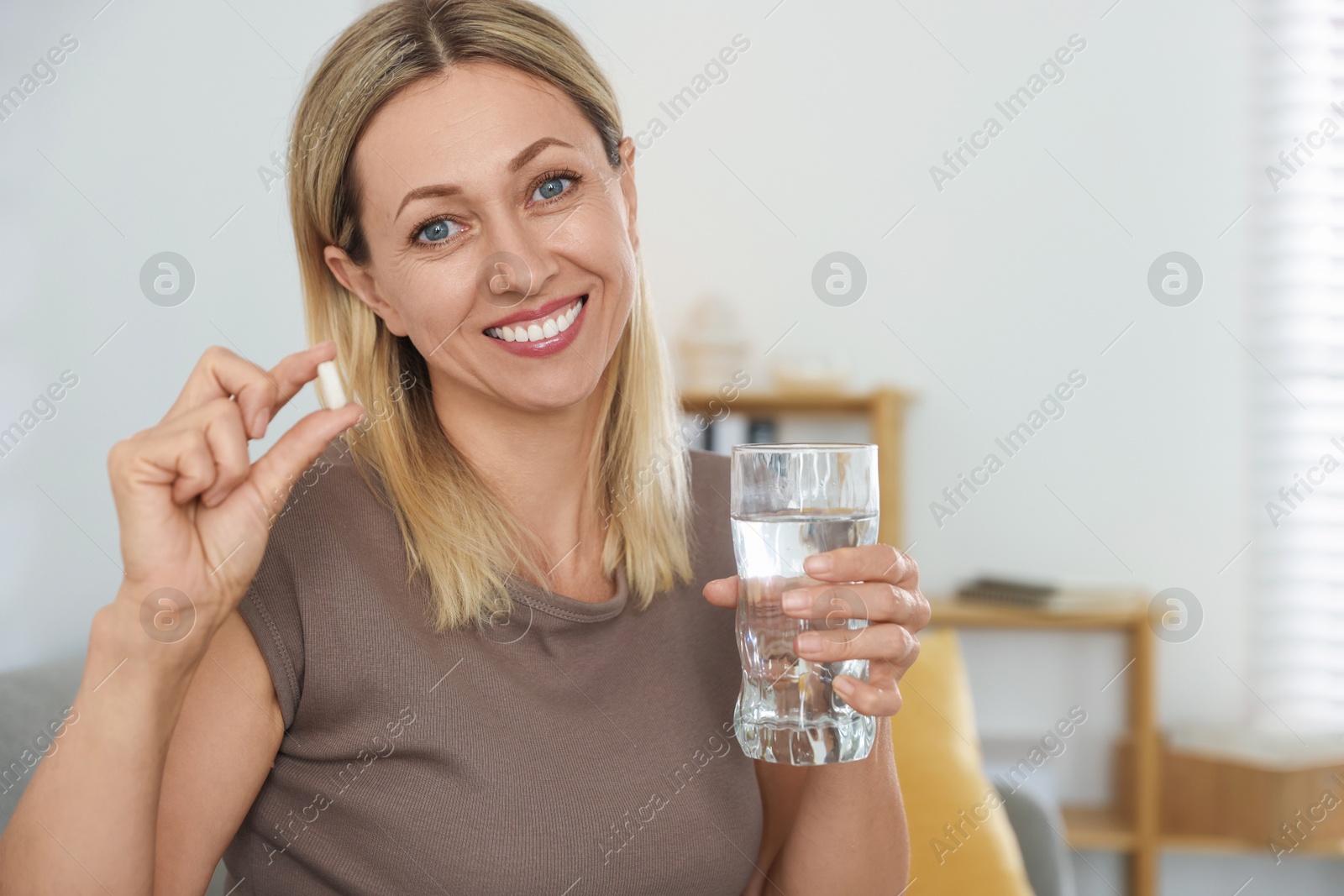 Photo of Menopause, hormone replacement therapy. Happy woman with glass of water and pill at home, space for text