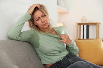 Photo of Menopause. Woman suffering from hot flash on sofa at home