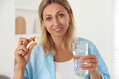 Menopause, hormone replacement therapy. Happy woman with glass of water and pill at home