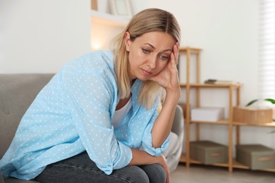 Photo of Menopause. Woman suffering from headache on sofa at home, space for text