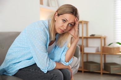 Photo of Menopause. Woman suffering from headache on sofa at home, space for text