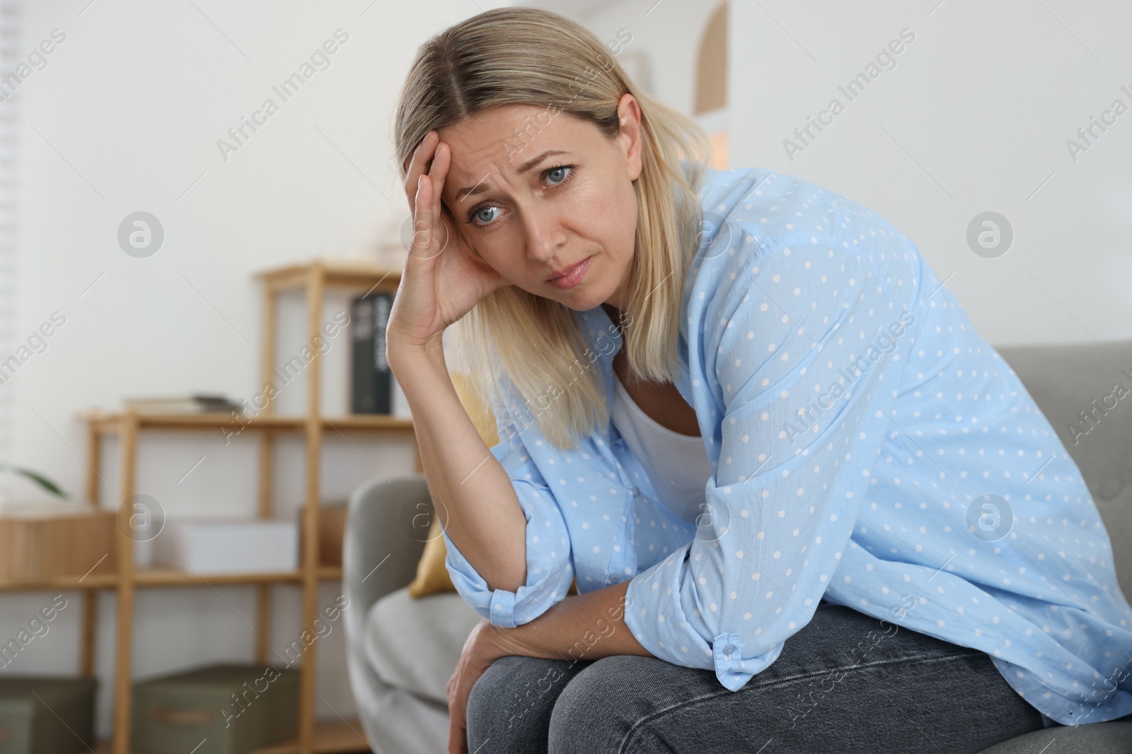 Photo of Menopause. Woman suffering from headache on sofa at home, space for text