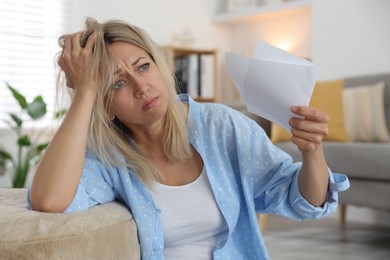 Menopause. Woman waving paper sheet to cool herself during hot flash at home