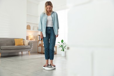 Photo of Menopause, weight gain. Concerned woman standing on floor scales at home