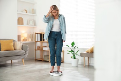 Photo of Menopause, weight gain. Concerned woman standing on floor scales at home