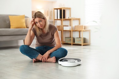 Photo of Menopause, weight gain. Concerned woman sitting near floor scales at home