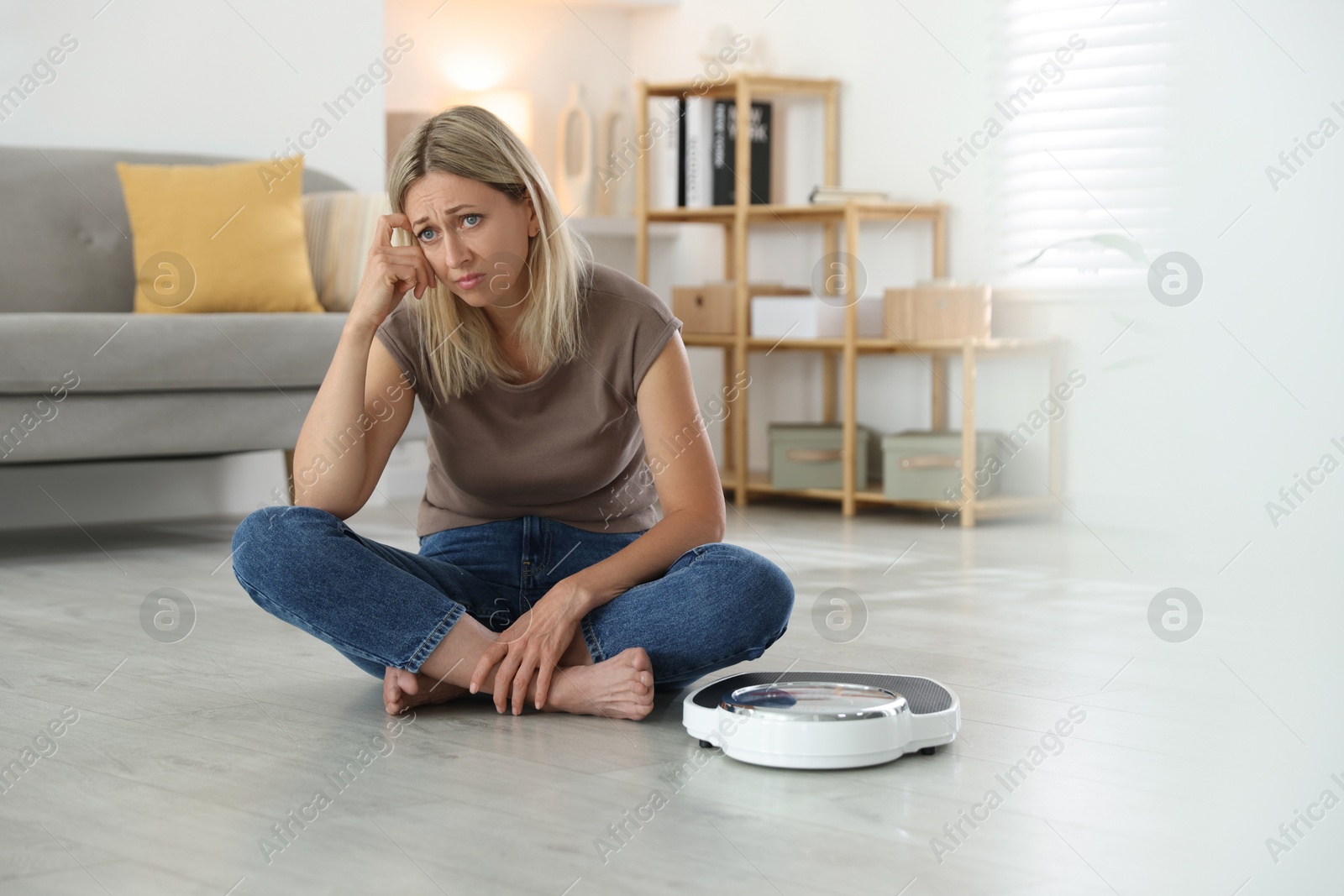 Photo of Menopause, weight gain. Concerned woman sitting near floor scales at home