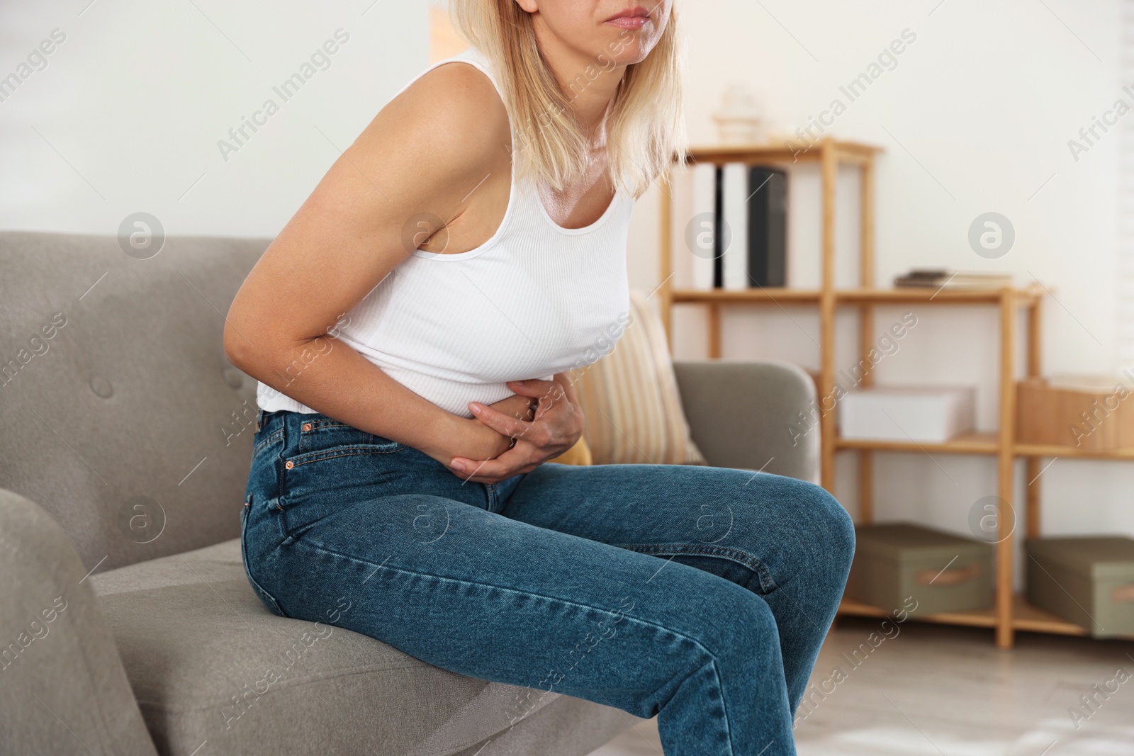 Photo of Menopause. Woman suffering from abdominal pain on sofa at home, closeup