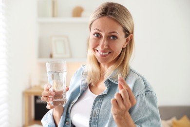 Menopause, hormone replacement therapy. Happy woman with pill and glass of water at home