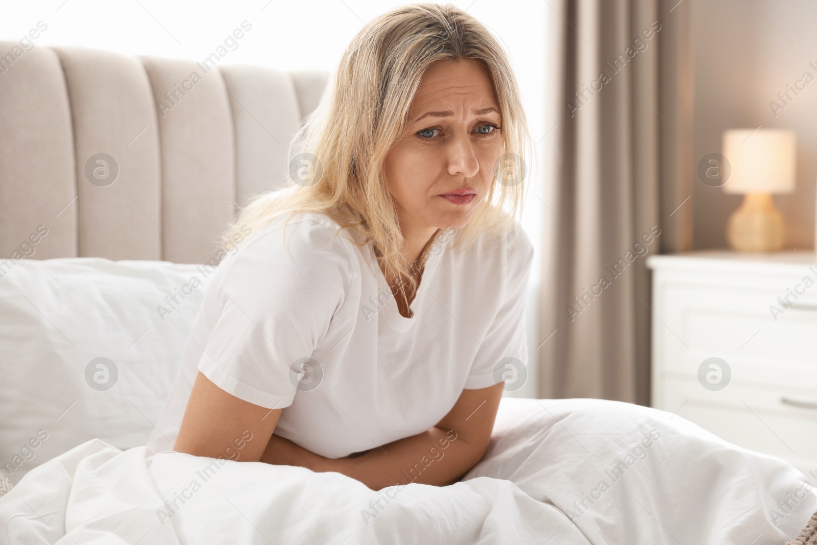 Photo of Menopause. Woman suffering from abdominal pain in bed at home