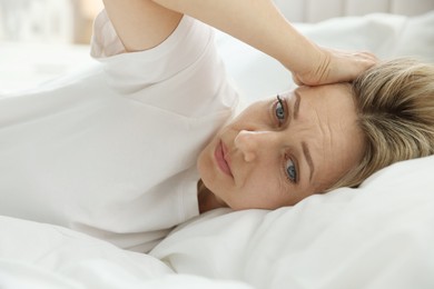 Photo of Menopause. Woman suffering from headache in bed at home