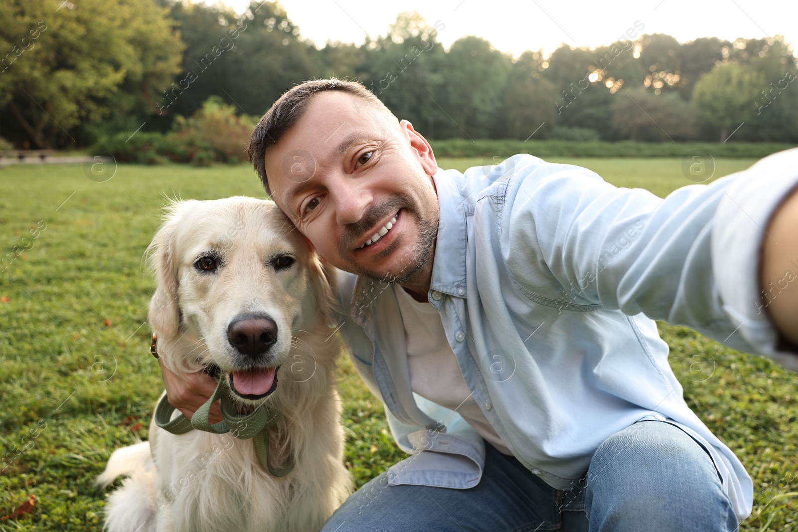 Photo of Smiling man with cute Golden Retriever dog taking selfie on spring day