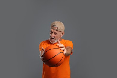 Photo of Portrait of emotional senior man with basketball ball on grey background