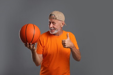 Photo of Portrait of senior man with basketball ball showing thumbs up on grey background