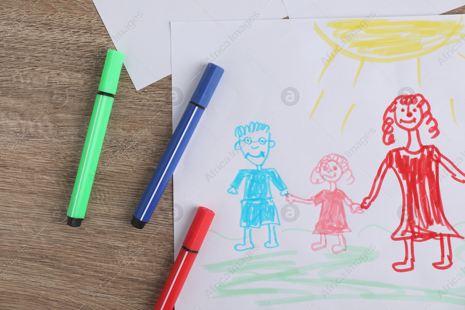 Photo of Child's drawing of happy family and felt tip pens on wooden table, top view