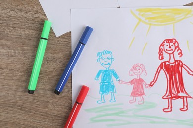 Photo of Child's drawing of happy family and felt tip pens on wooden table, top view