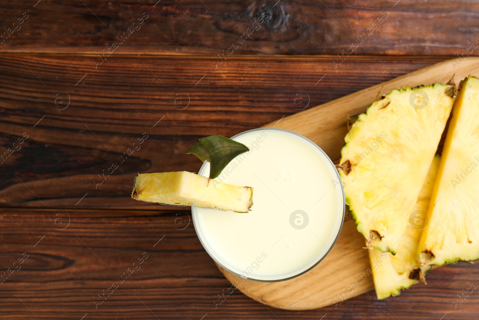 Photo of Board with tasty pineapple smoothie in glass and slices of fruit on wooden table, top view. Space for text