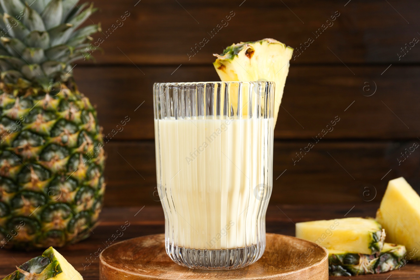 Photo of Tasty pineapple smoothie in glass and slices of fruit on wooden table, closeup